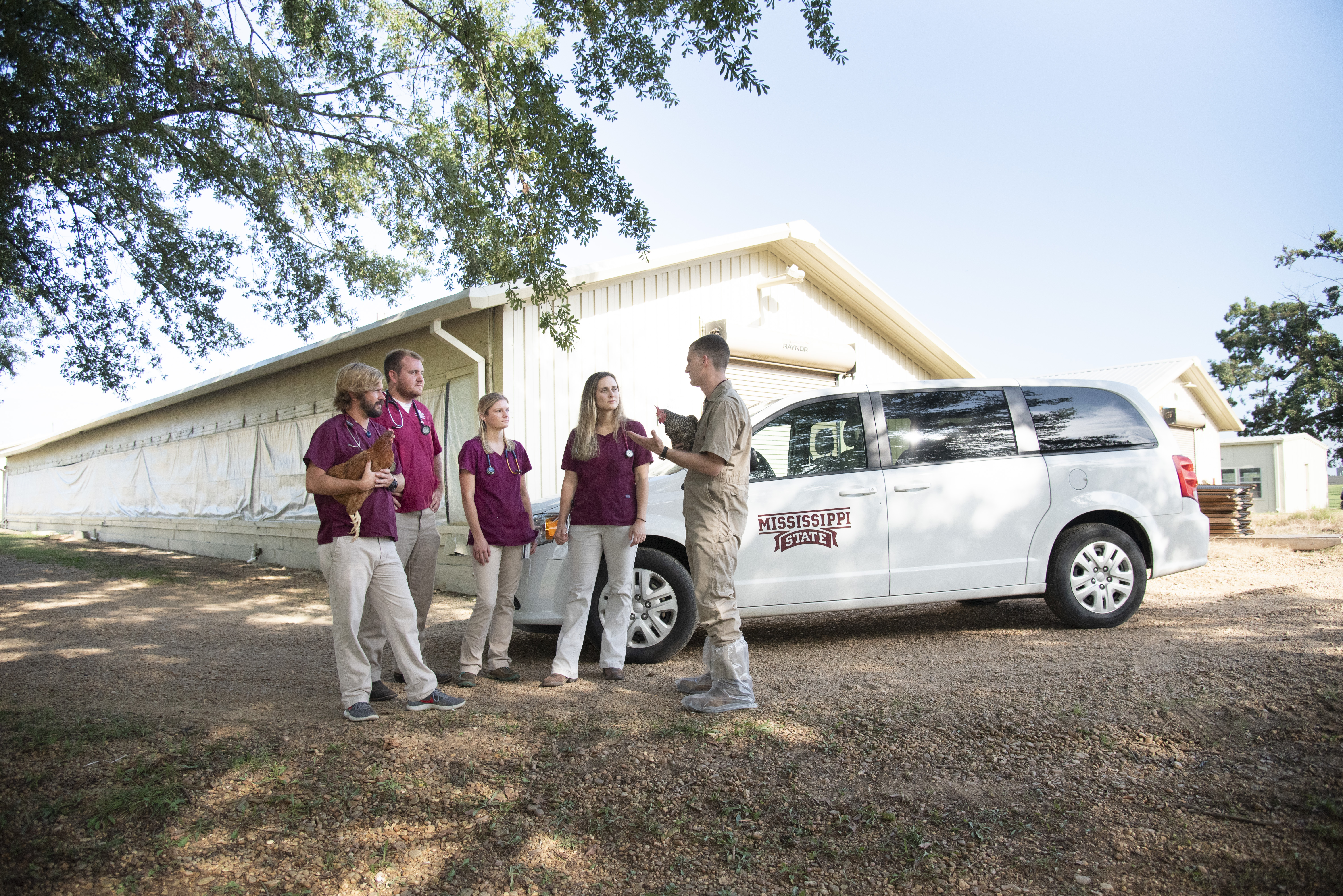 People in maroon scrubs talk outside of a chicken house